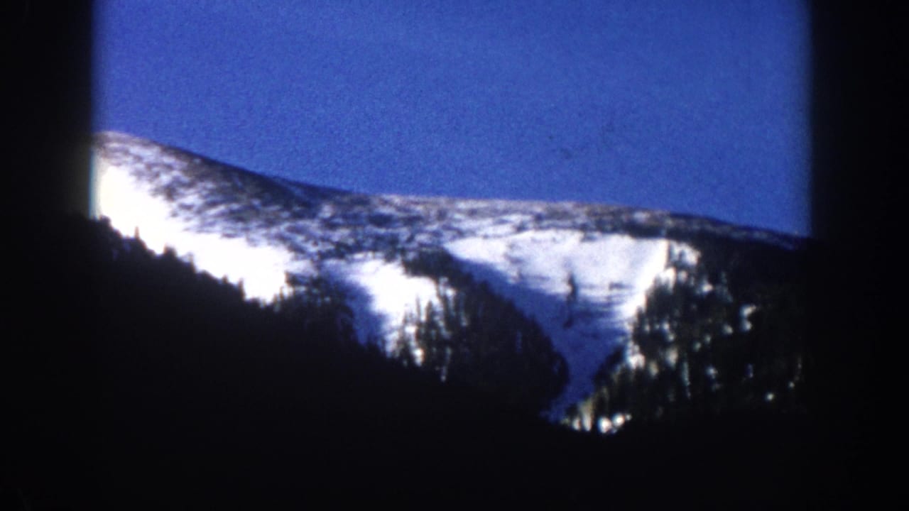 8mm home movie frame showing a snow-capped Rocky Mountain slope against deep blue sky, circa 1961, with heavy vignette borders