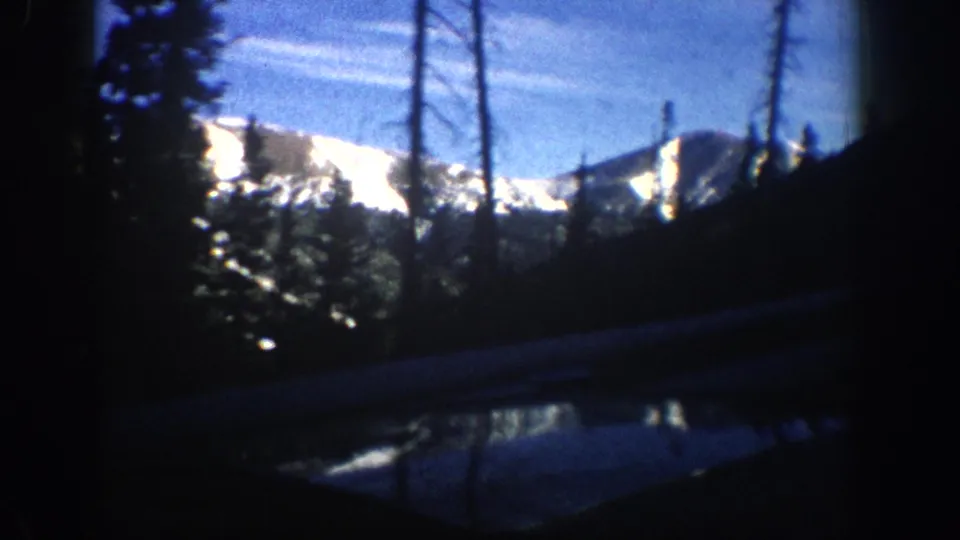 8mm travel footage showing silhouetted conifers and sunlit snow-capped peaks, consistent with Colorado Rockies area, circa 1961.
