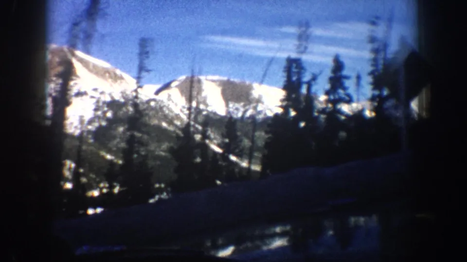 8mm travel footage showing a dominant snow-covered rocky peak and silhouetted pines above a mountain road, Aspen, Colorado area, circa 1961.