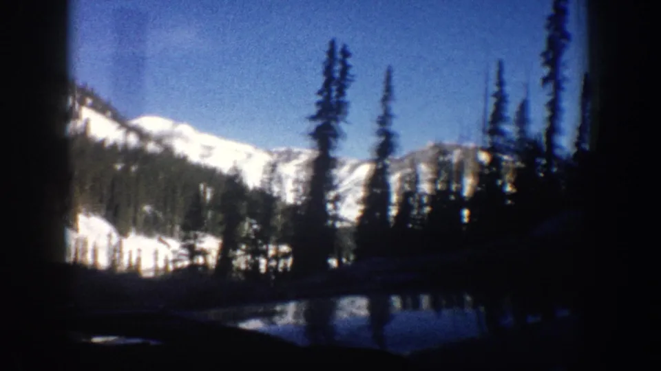 8mm amateur travel footage, likely Aspen, Colorado, 1961, showing a snowy mountain ridge and dense conifers through a car window, with lower valley terrain visible.