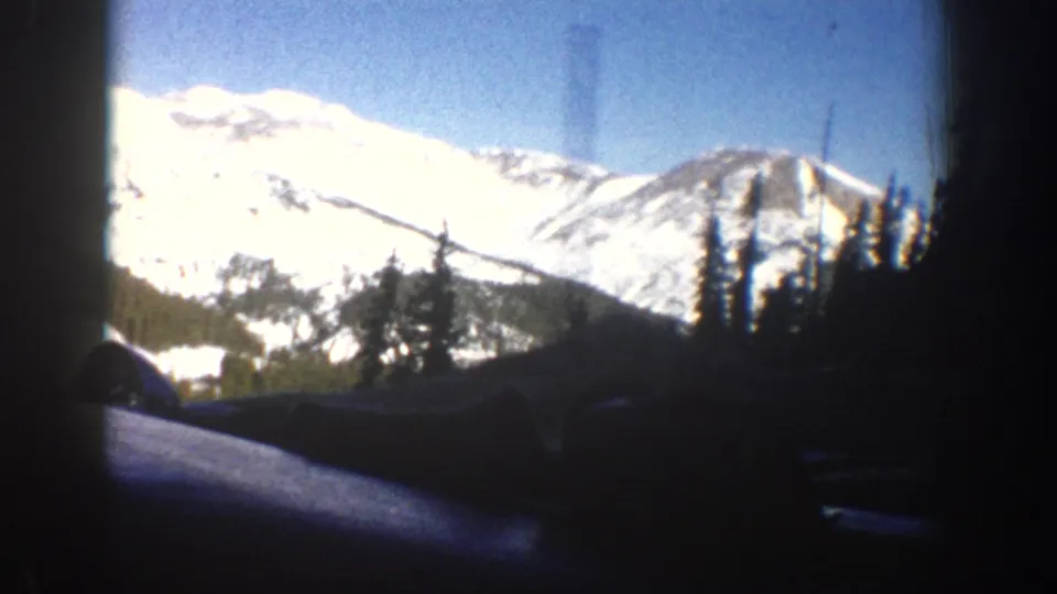 8mm footage from the Aspen, Colorado area, 1961, showing a broad snow-covered mountain face with sparse evergreen trees; car window frame visible at left edge.