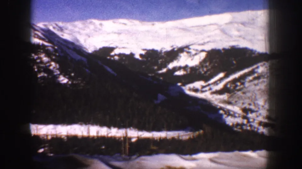 Moving-vehicle shot of snow-covered mountain slope and valley near Aspen, Colorado, circa 1961, on 8mm film.