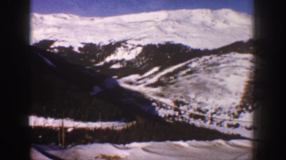 8mm film view of snow-covered Rocky Mountain slopes and valley near Aspen, Colorado, circa 1961, with bare foreground trees.