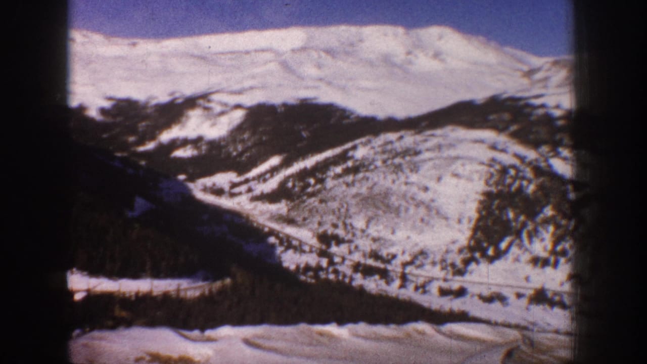 8mm pan across snow-covered Rocky Mountain ridge near Aspen, Colorado, circa 1961, with valley road and conifer-forested slopes.