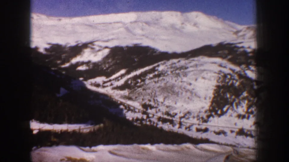 8mm pan across snow-covered Rocky Mountain ridge near Aspen, Colorado, circa 1961, with valley road and conifer-forested slopes.