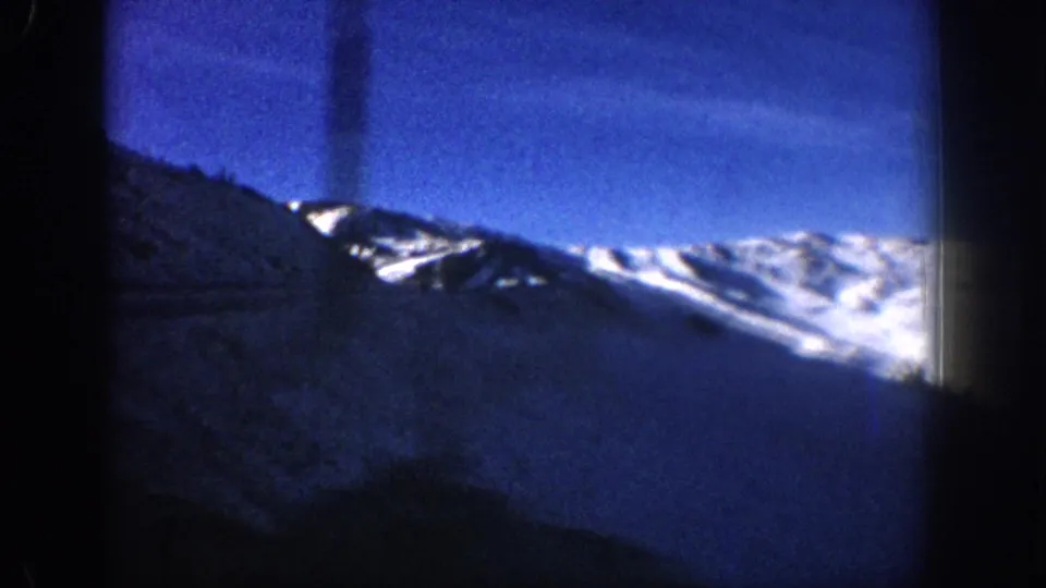 8mm home movie pan frame showing a snowy ridge against blue sky with a visible vertical film-scratch artifact, Aspen area, circa 1961.
