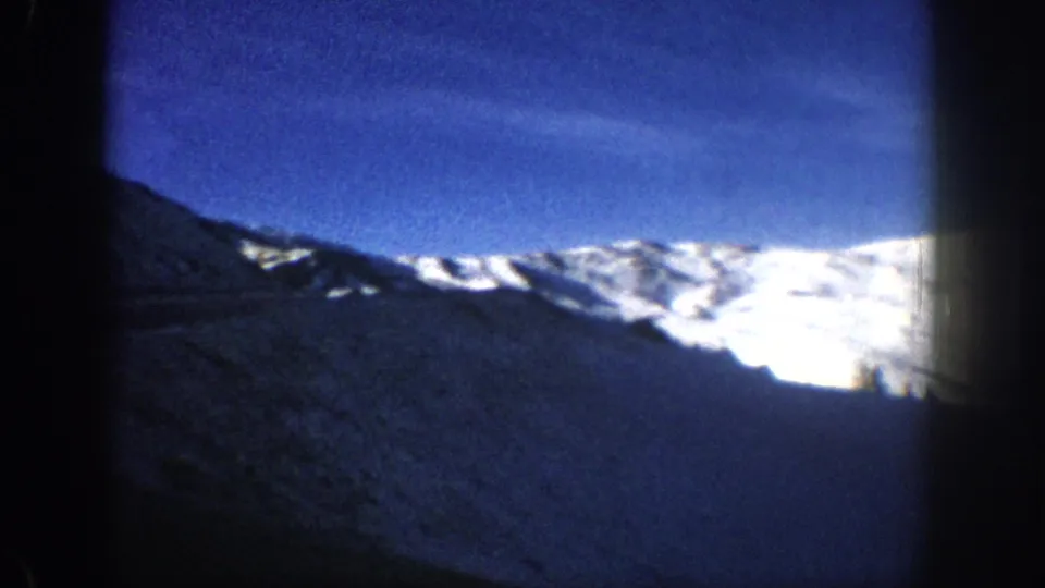 Final pan frame of 8mm home movie showing a snow-bright mountain slope and blue sky with a right-edge light flare, Aspen area, circa 1961.