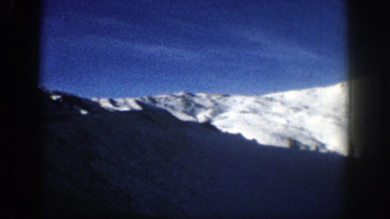 Brightly sunlit snow-covered mountain peak against deep blue sky, filmed from a moving vehicle on a Colorado mountain road, circa 1961, 8mm.
