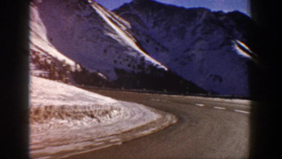 8mm home movie, circa 1961, of a sweeping road bend through a snowy Colorado mountain pass with a color shift visible on the distant ridgeline.