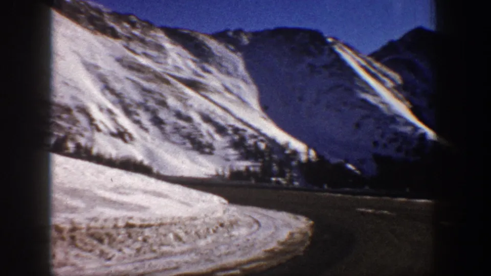 8mm home movie frame, circa 1961, showing steep snow-laden Colorado slopes under a vivid blue sky, with chromatic aberration fringing the bright ridgeline.