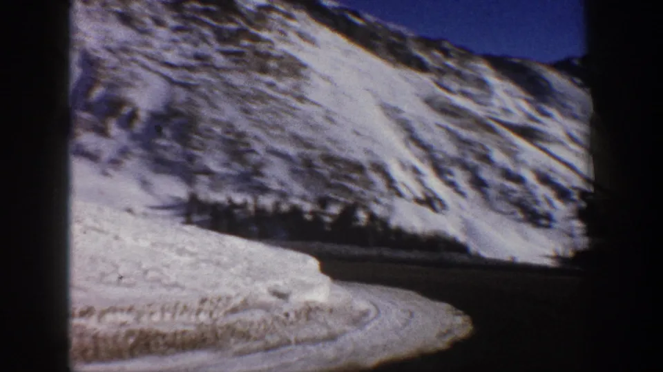 8mm home movie frame, circa 1961, showing a close perspective on snow-covered Rocky Mountain terrain with motion blur suggesting continued vehicle movement.