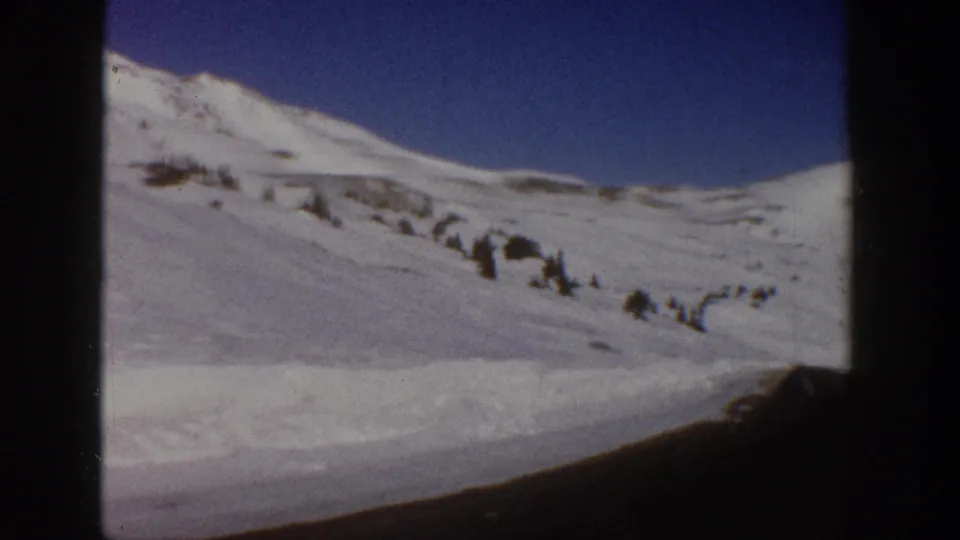 8mm frame c.1961 showing open snow-covered slopes above a winding road at high elevation, consistent with a Colorado mountain pass in winter.