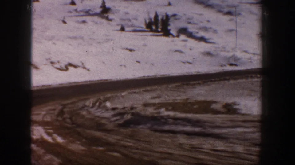 8mm film frame circa 1961 showing a snow-covered Colorado hillside with conifer clusters and broad open snowfields in soft winter light.