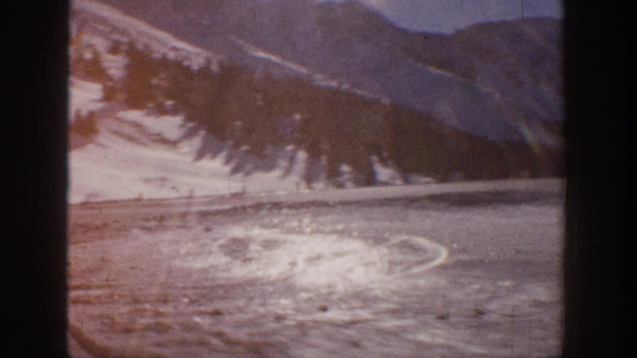 Frozen lake surface with swirling ice patterns, a road at its edge, and warm-toned snow-covered mountains behind.