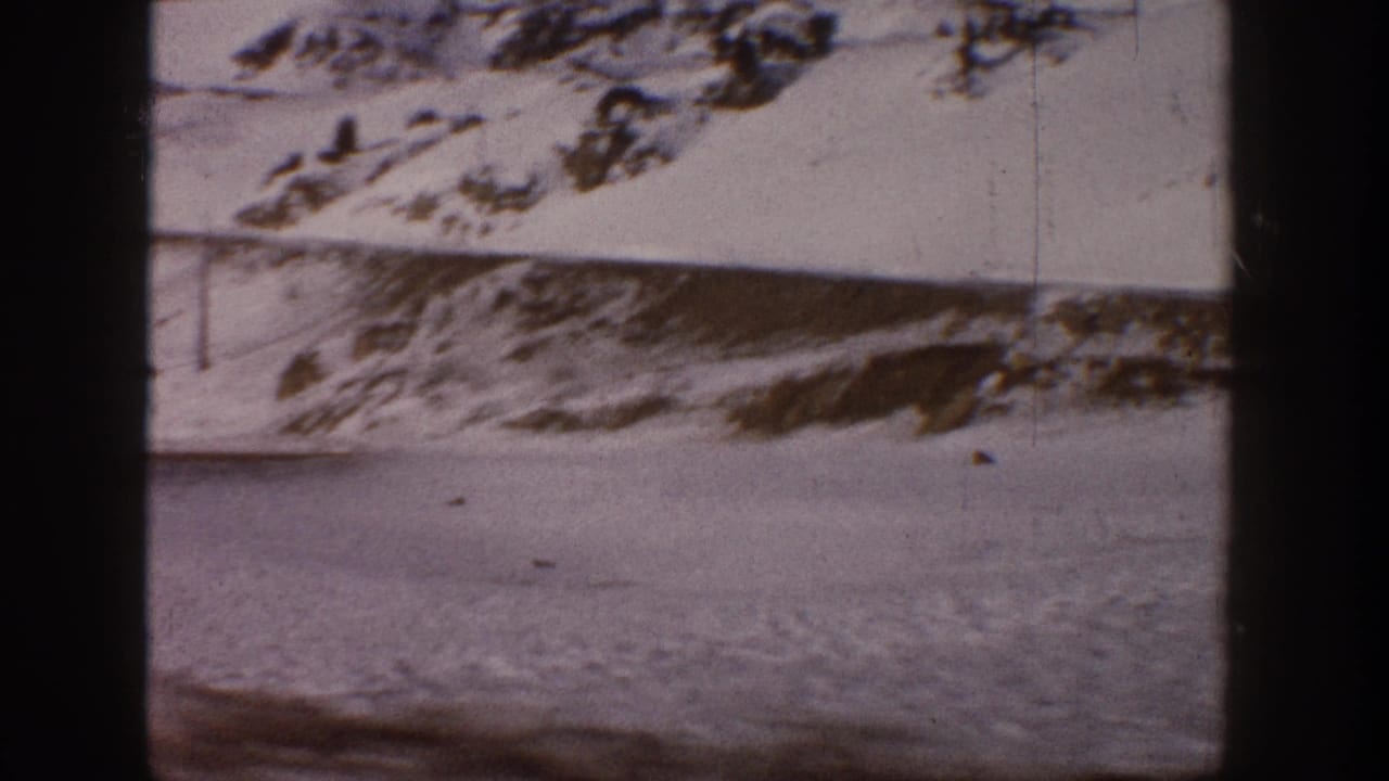 Panning view of snow-covered mountain ridgeline with flat snowy terrain below, 8mm film with dark border.