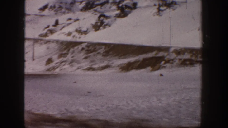 1961 Aspen, Colorado: continued pan across snow-covered mountain slopes and flat snowy terrain below, 8mm home movie footage with visible grain and edge vignette.