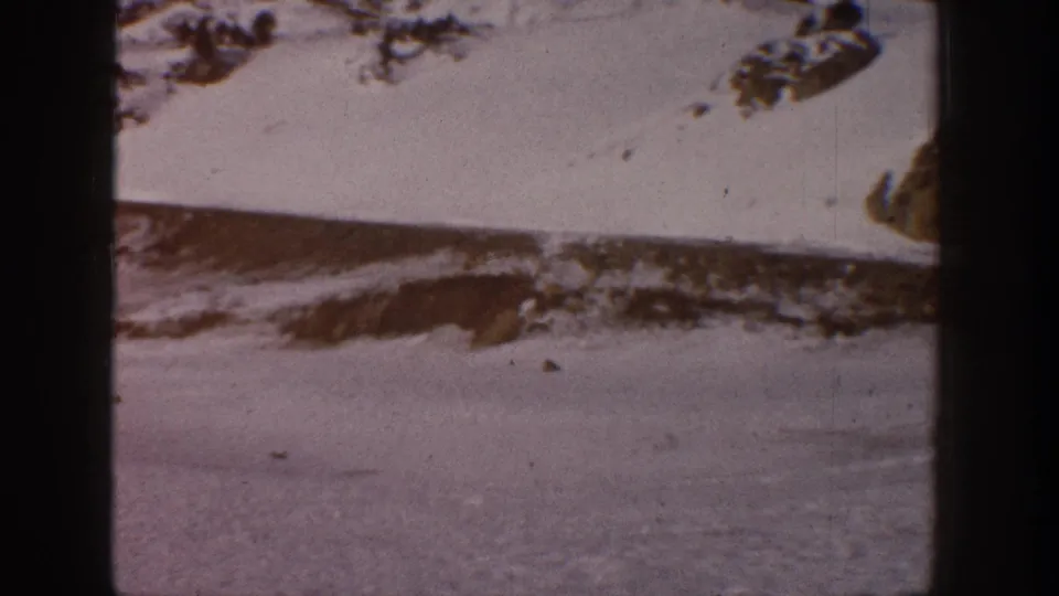 Snowy mountain landscape possibly in Aspen, Colorado, 1961, with a dark foreground or mid-ground object that may be a vehicle; 8mm home movie film with grain and edge vignette.