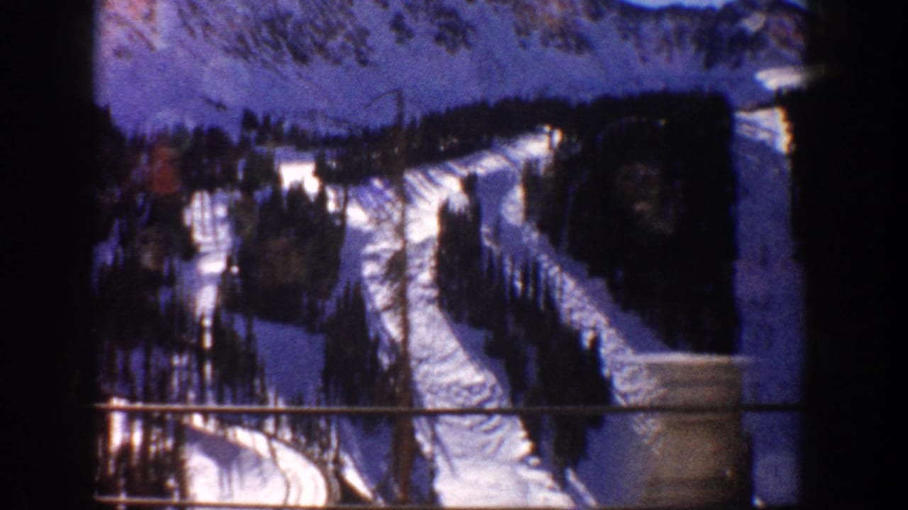 8mm home movie frame circa 1961, likely Aspen, Colorado, showing ski slopes and conifer forest from a moving chairlift or vehicle window.