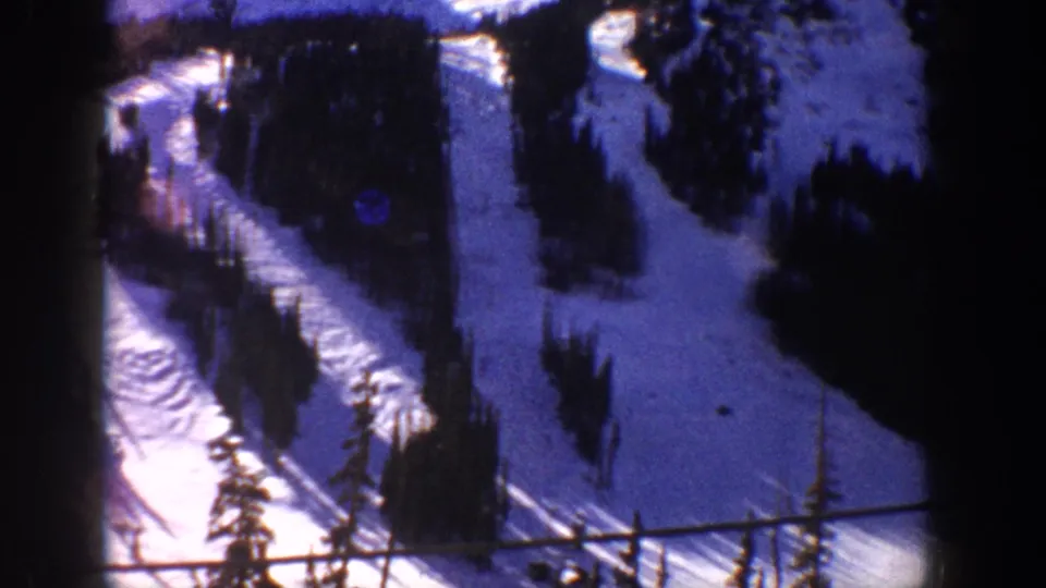 8mm home movie frame circa 1961 showing forested ski slopes at a Colorado mountain resort, captured from an elevated moving vantage through a vehicle or lift window.