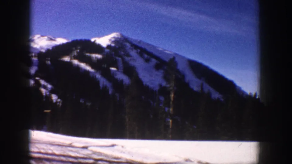 8mm shot of a sharp snow-covered mountain peak with what appears to be a ski slope visible, photographed through a moving vehicle window, Aspen area, circa 1961.