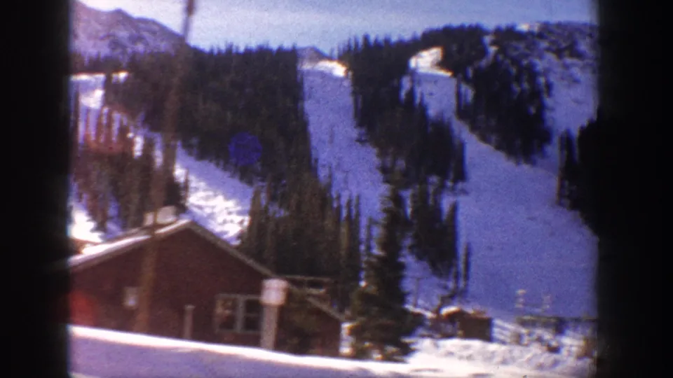 8mm home movie frame of a red lodge building and snowy mountain ski slopes, Aspen, Colorado, 1961; light flare artifact visible at the right edge of the frame.