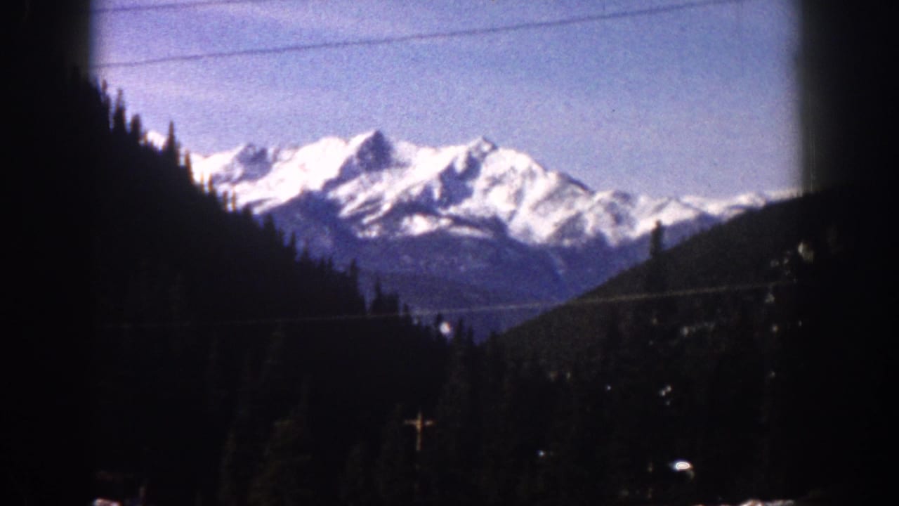 Snow-capped Rocky Mountain peaks shot through a vehicle window with visible window-edge vignette, Aspen, Colorado area, circa 1961, 8mm film.