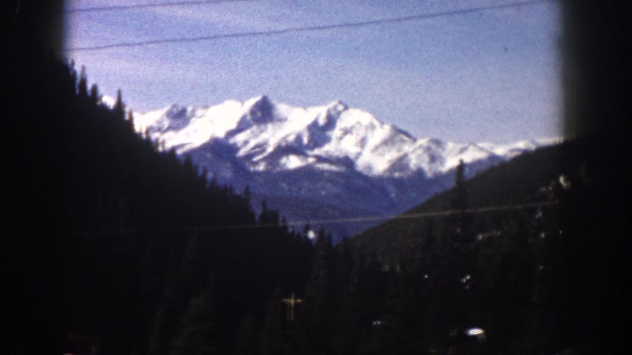 Same mountain range from car window at a slightly shifted angle, utility lines and dense pines visible, right-side window vignette.