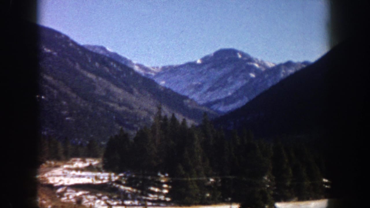 8mm film frame, c. 1961, showing snow-capped peaks rising above a conifer-forested valley with snow on the floor, likely Aspen area, Colorado.