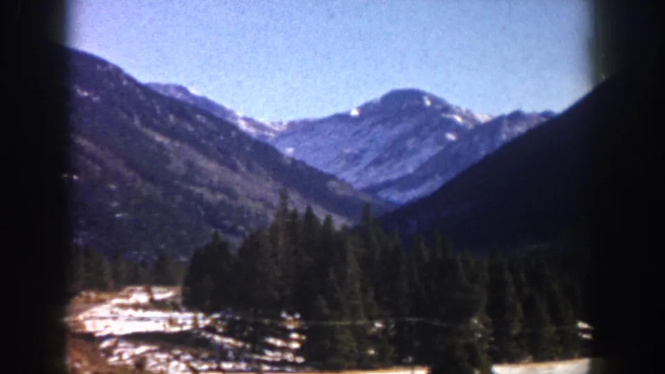 8mm film frame, c. 1961, Aspen area, Colorado: mountain valley composition showing snow-capped peaks and dense conifer forest with snow on the valley floor.