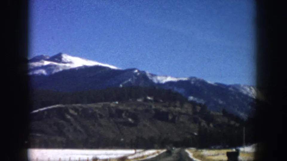 8mm road-trip frame, Aspen-area Colorado, c.1961 — mountain panorama from moving vehicle with flat valley visible in foreground.