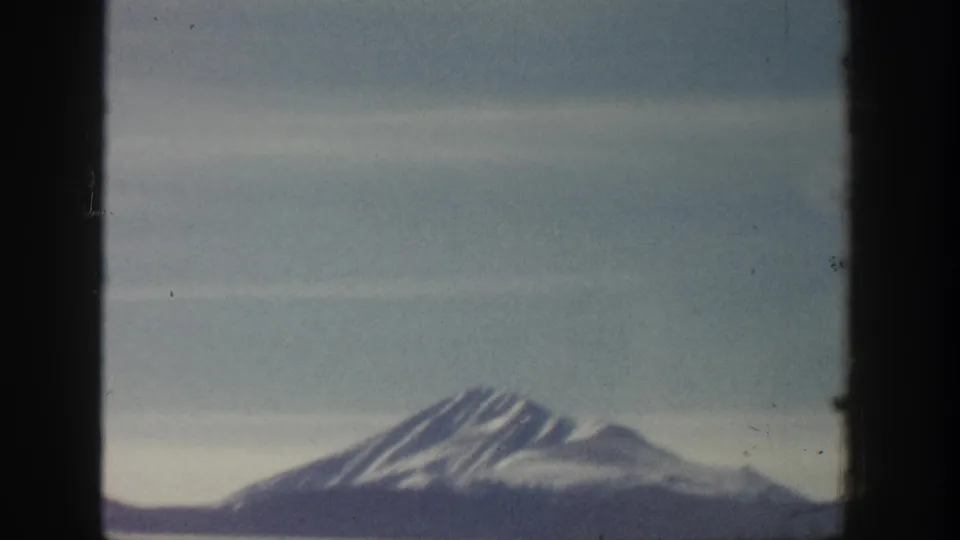 8mm home-movie frame showing a snow-covered peak, possibly in the Aspen area of Colorado circa 1961, with muted color palette from film aging.