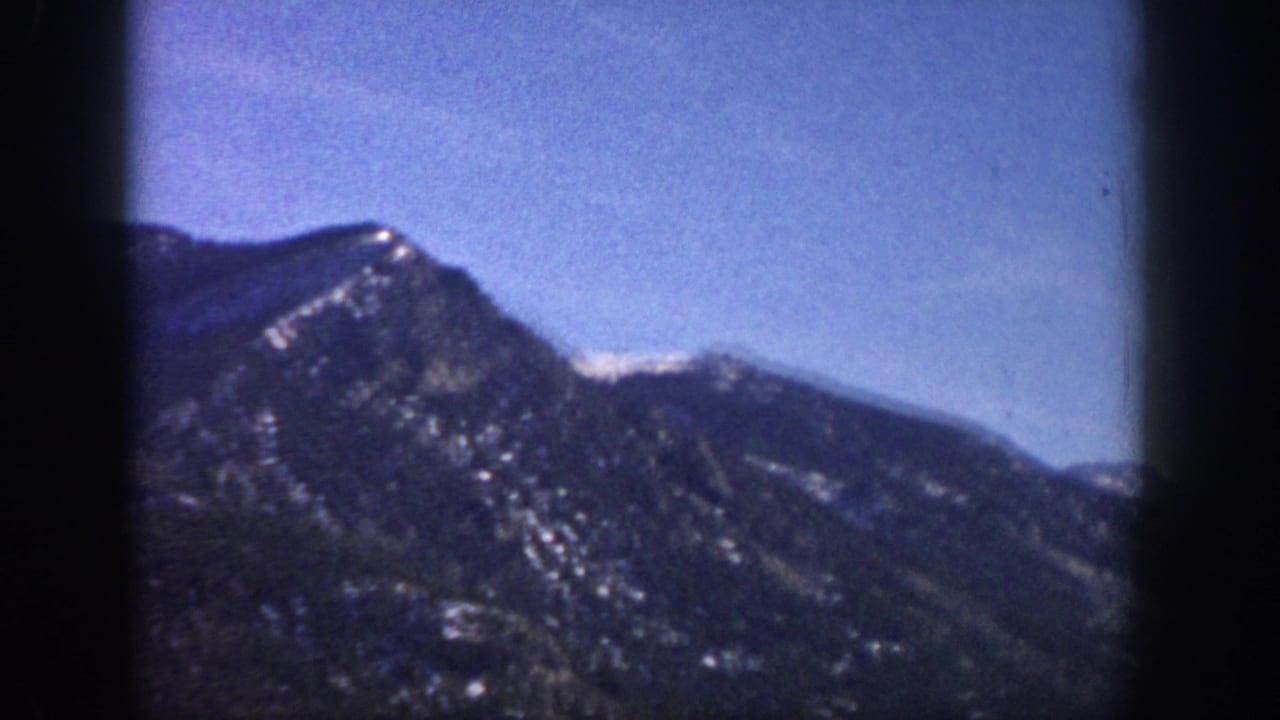 8mm close shot of a forested mountain slope with snow patches on the upper ridge, attributed to the Aspen, Colorado area, 1961.
