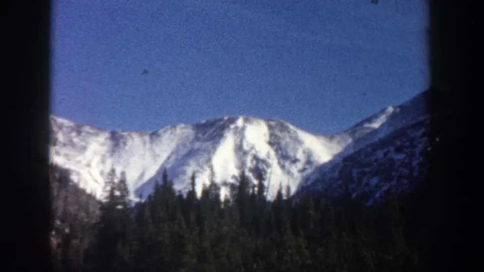 Wide 8mm shot of snow-capped Colorado mountain peaks above a forested valley floor, attributed to the Aspen area, circa 1961.