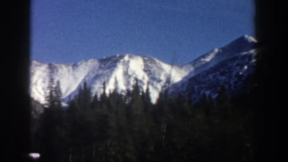Concluding 8mm pan frame of snow-covered Colorado mountain peaks with conifer forest foreground, Aspen area, circa 1961.