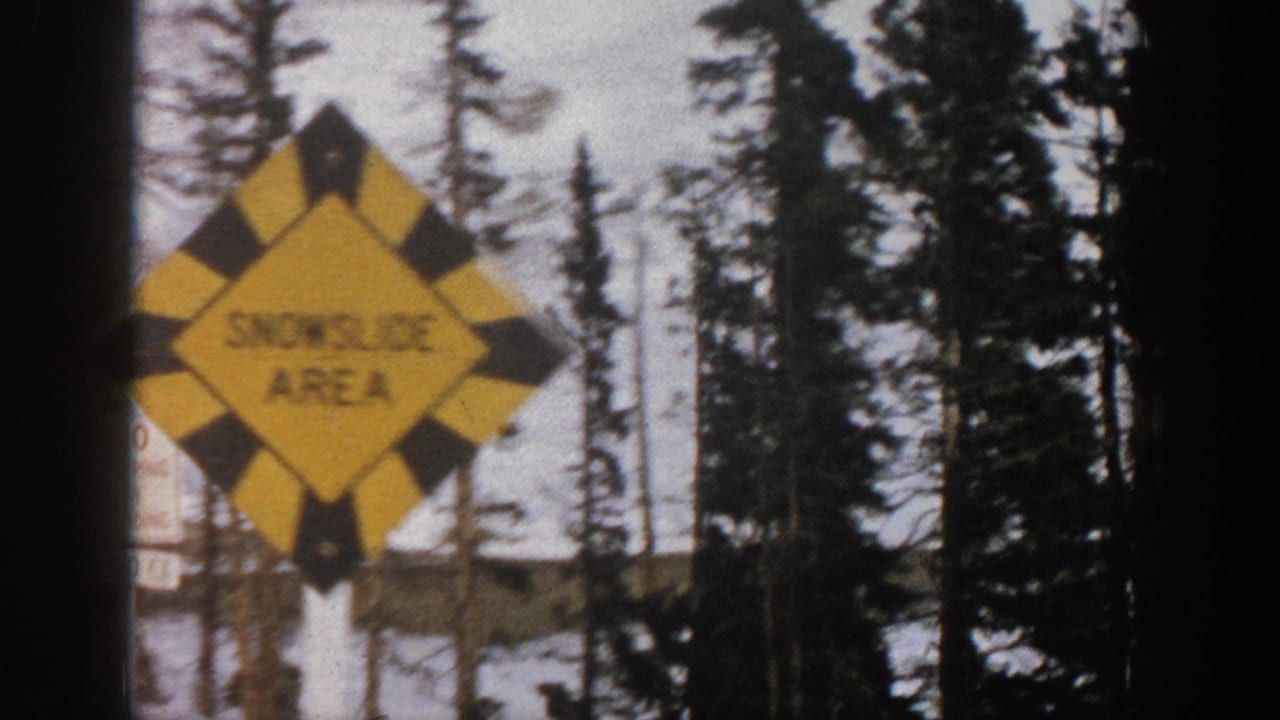 Yellow snowfall-area warning sign beside snowy trees and mountains.