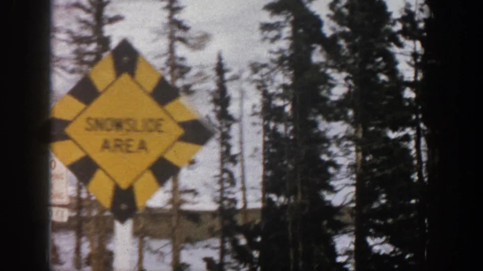 Yellow snowfall-area road sign in a snowy Aspen-area mountain setting, filmed on 8mm from a moving vehicle.