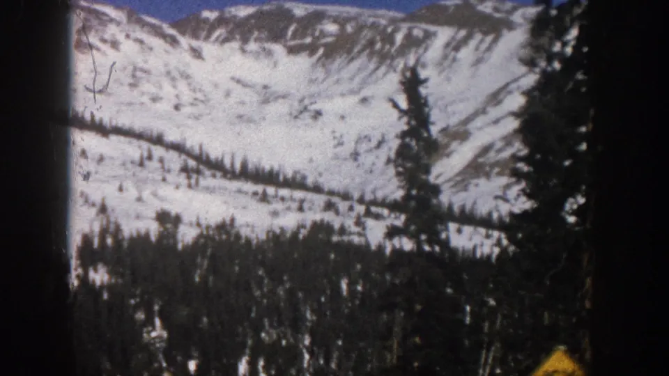 Wide 8mm view of snow-covered mountain terrain and evergreen forest in the supplied 1961 Aspen, Colorado road-trip footage.