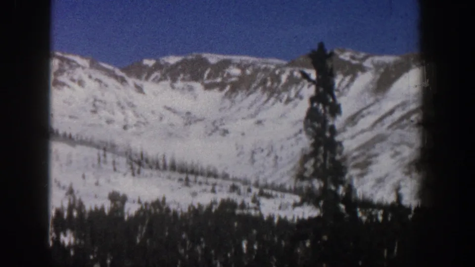 Snowy Aspen-area mountain ridge and foreground evergreens captured in grainy 8mm home-movie footage from 1961.
