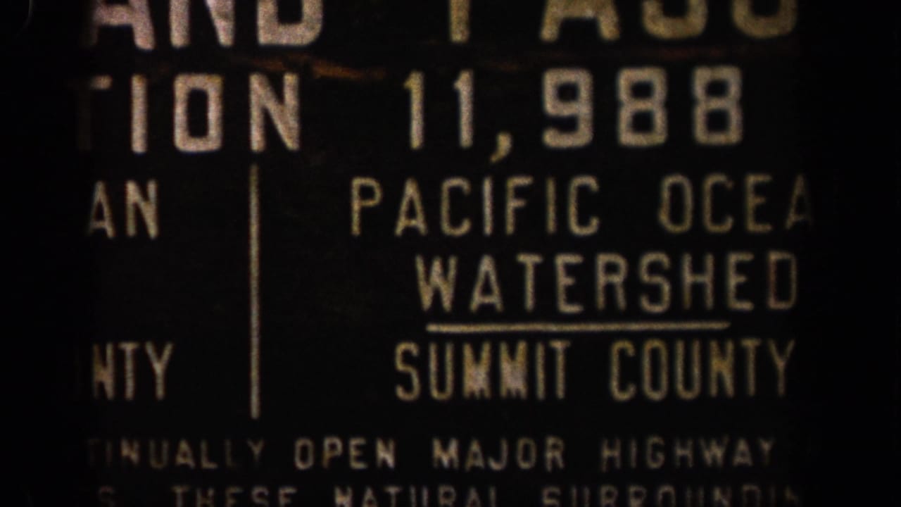 1961 Colorado 8mm frame showing a dark roadside sign reading Pacific Ocean Watershed and Summit County in cropped view.