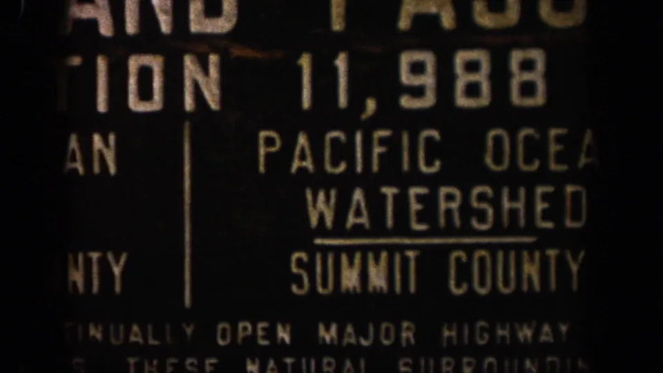 1961 Colorado 8mm frame showing a dark roadside sign reading Pacific Ocean Watershed and Summit County in cropped view.