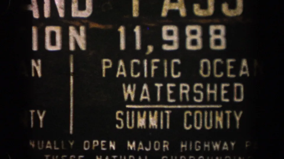 1961 Colorado 8mm frame showing a readable roadside sign detail for the Pacific Ocean Watershed in Summit County.