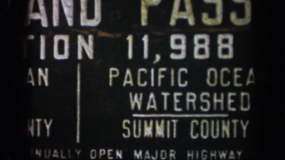 1961 Colorado home-movie frame with the Pacific Ocean Watershed wording and Summit County label visible on a roadside sign.
