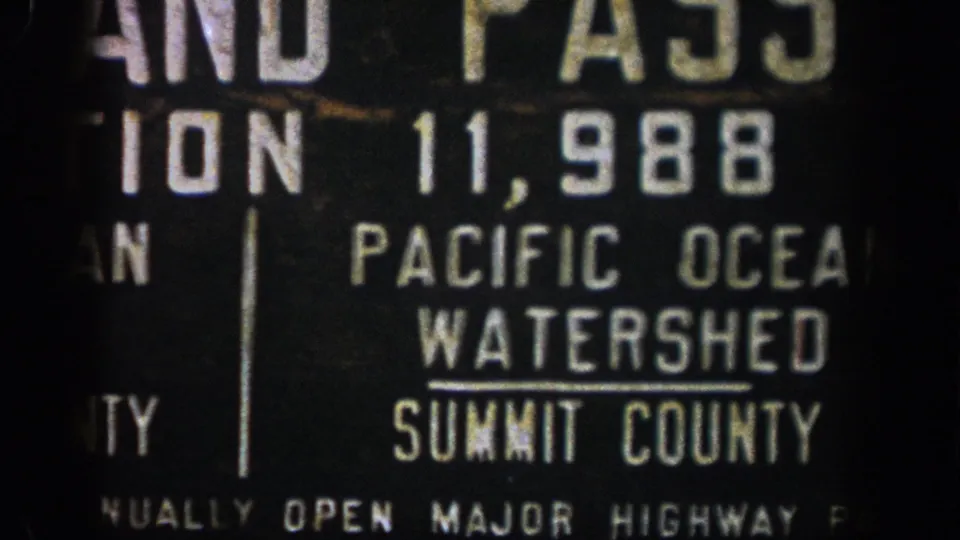 1961 Colorado travel footage frame showing the Summit County Pacific Ocean Watershed sign cropped tightly in 8mm grain.