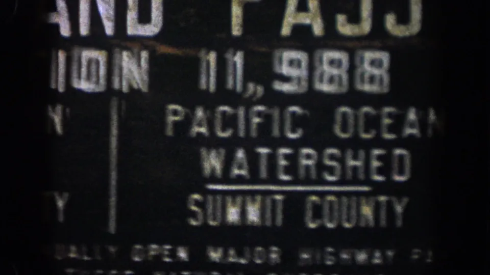 1961 Colorado 8mm frame of a dark roadside Pacific Ocean Watershed sign with Summit County text visible.