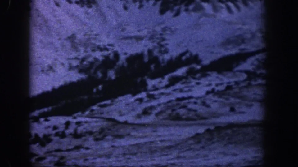 1961 Aspen-area home-movie frame showing a broad snowy mountainside, dark tree line, and road through the alpine landscape.
