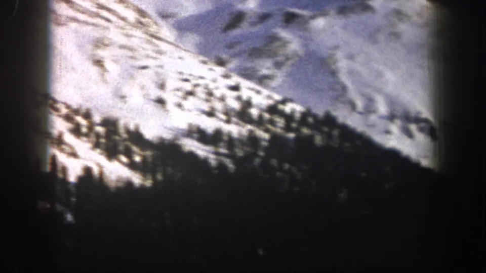 1961 Aspen home-movie frame of a snow-covered mountain flank with scattered conifers and dark shadowed foreground.