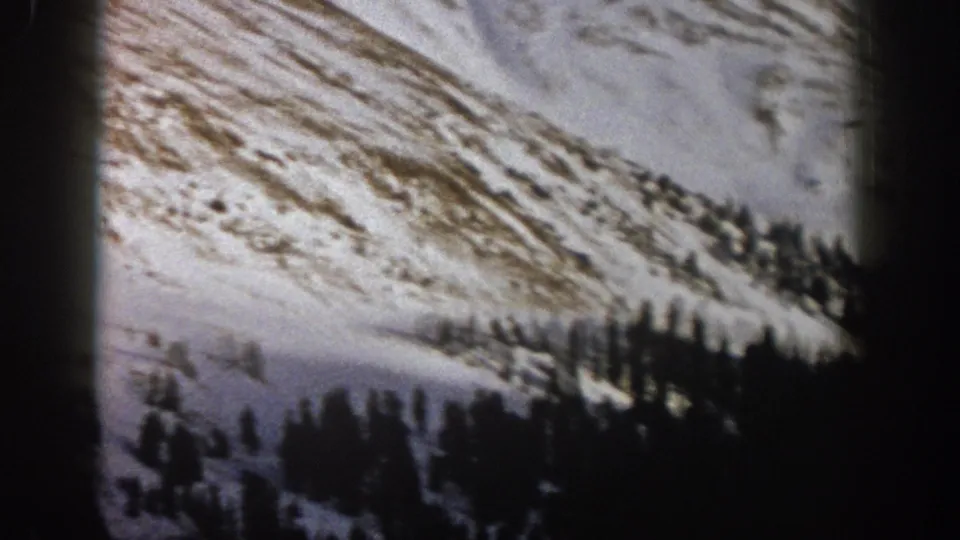 Aspen, Colorado 1961 frame showing a snow-striped mountainside, evergreen clusters, and a pale open slope or path below.