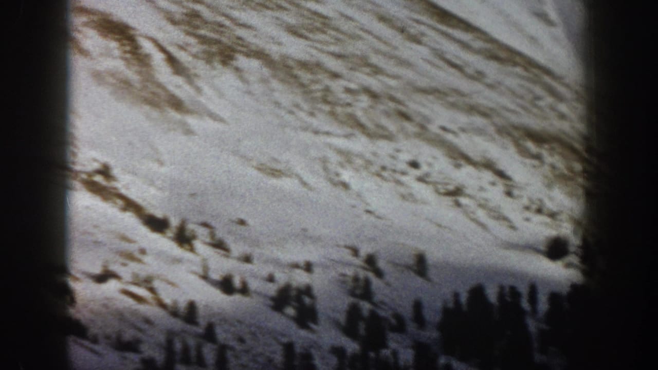 1961 Aspen-area 8mm frame showing a snow-covered mountain slope with dark evergreen trees and patches of exposed earth.