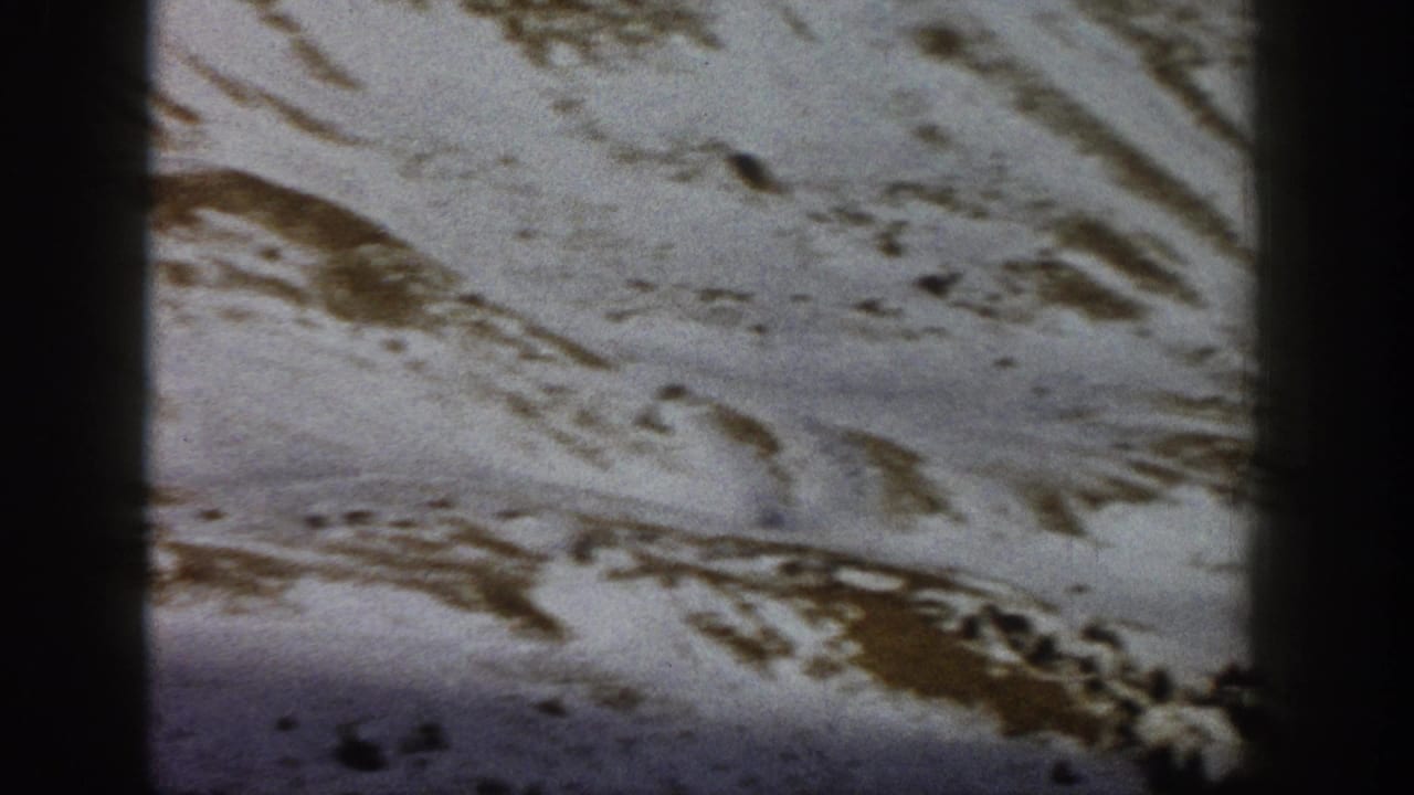 1961 Aspen-area home-movie frame of a snowy hillside with irregular exposed ground and sparse evergreen forms.