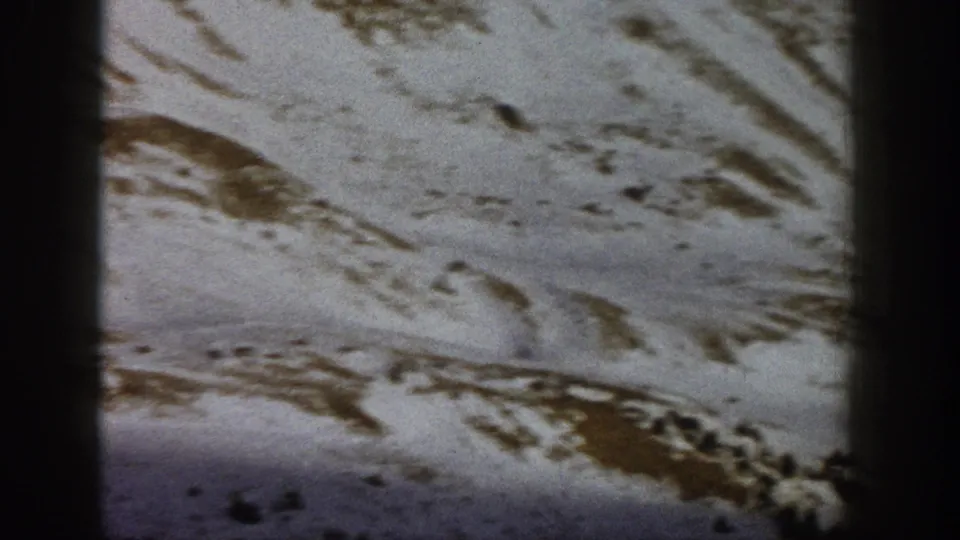 1961 Aspen-area home-movie frame of a snowy hillside with irregular exposed ground and sparse evergreen forms.